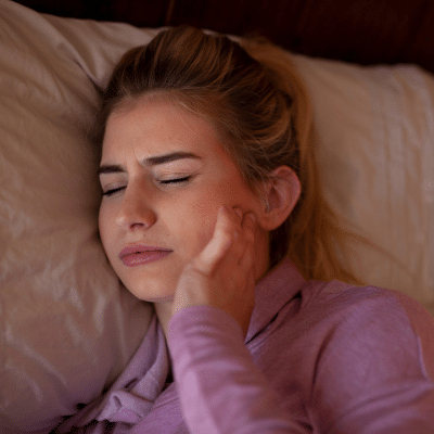 Tmj treatment: finding relief for jaw pain in charlotte, nc 11 Woman in bed holding jaw, representing tmj treatment