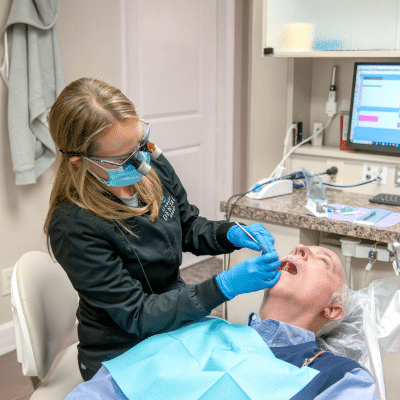 How to know if you need a root canal: signs you shouldn’t ignore 3 Dr. Melissa stewart wearing a mask and gloves while examining a man's teeth, representing how to know if you need a root canal