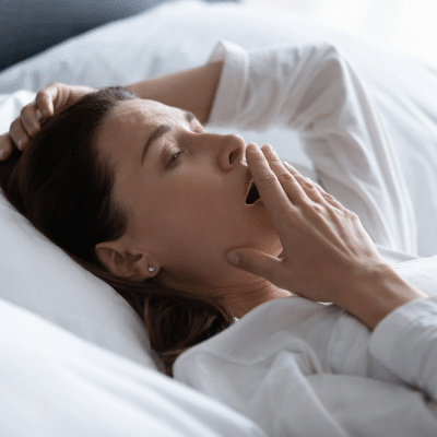 Understanding the types of sleep apnea 3 Woman yawning in bed, looking tired, representing the different types of sleep apnea